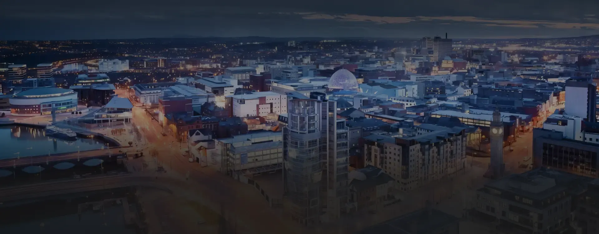 Belfast city centre at dusk — streets glowing amber against a deep blue sky