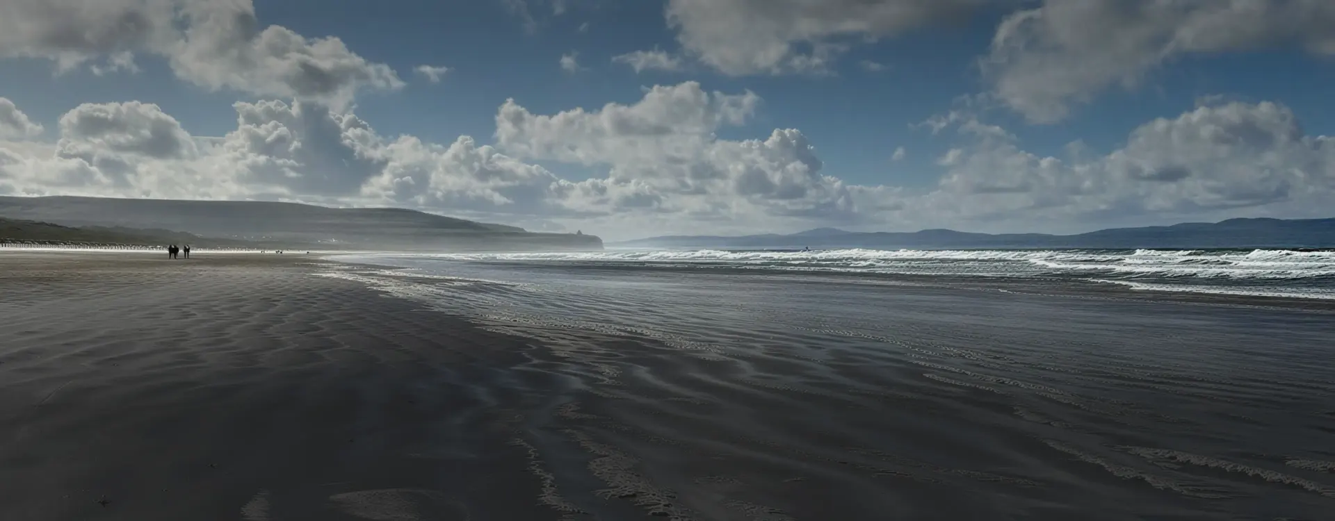 Wide beach under dramatic clouds with waves rolling in